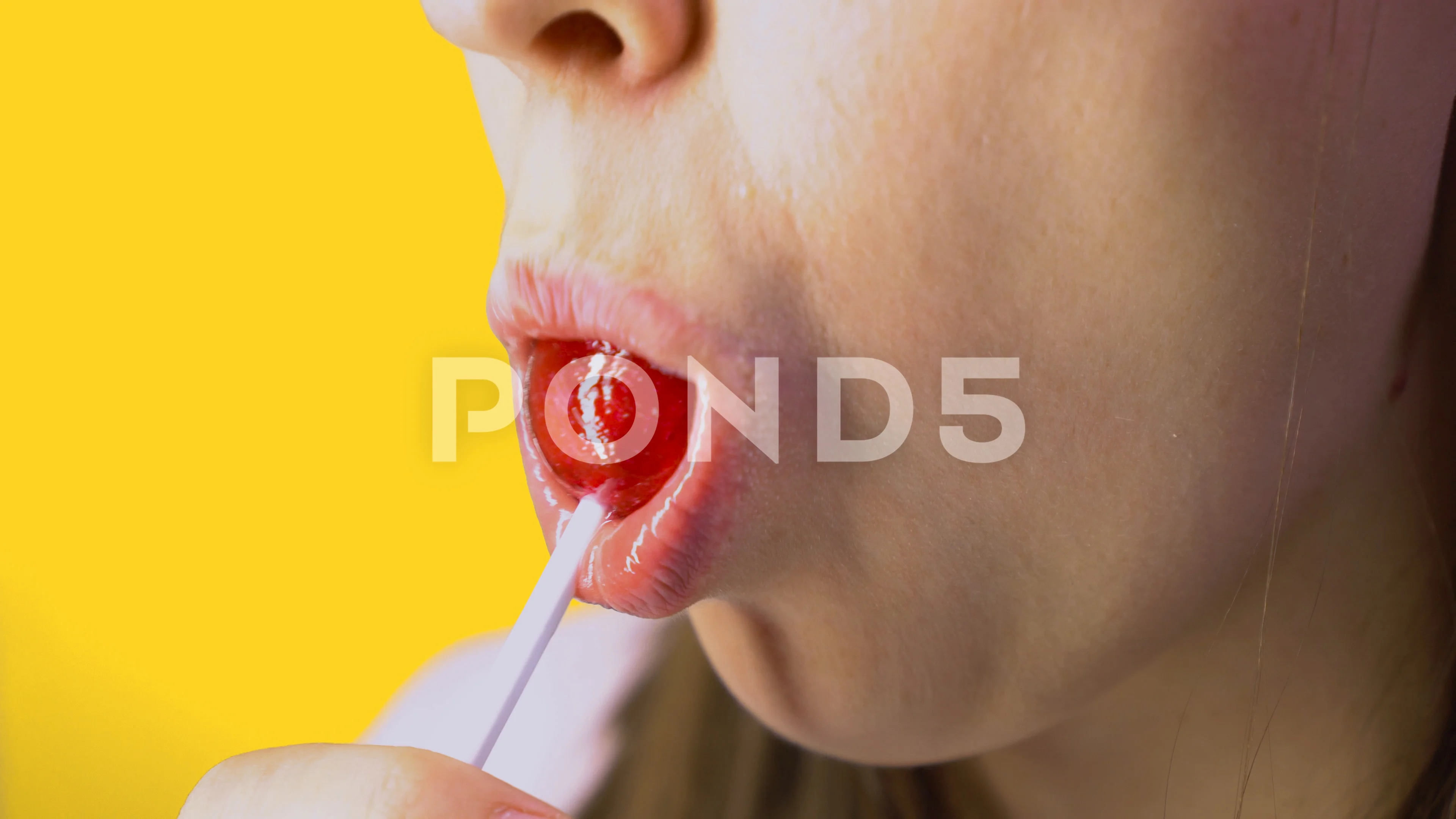 Close-up, female sexy lips suck big pink round lollipop. Yellow background