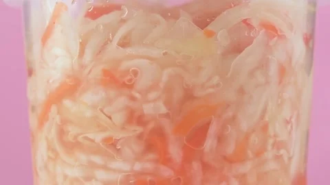 Close up of fermented cabbage and carrot salad turning in jar against pink Stock Footage 332172483