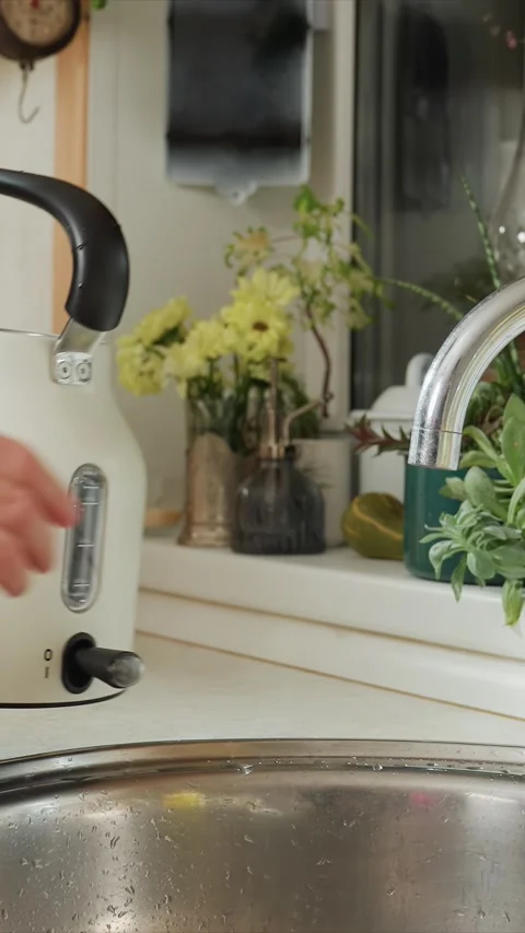 Close up filling cream colored kitchen kettle under running faucet with visible Stock Footage 344420896