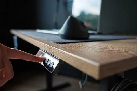 Close up of finger pressing control button on electric adjustable desk with w Stock Photos