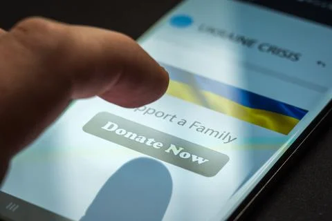 Close-up finger pressing donate button on smartphone screen. Donation money 库存照片