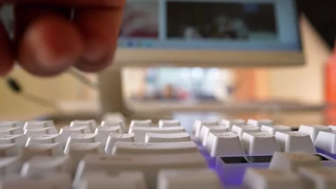 Close-up of a finger pressing a key on a white keyboard with a blurred moni.. Stock Footage 320724968