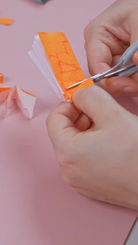 Close up of fingers guiding small scissors through folded orange tissue layer Stock Footage 347105130