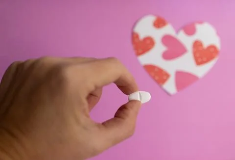 Close-up of fingers holding a pill. Background with blurred heart figure Stock-Fotos