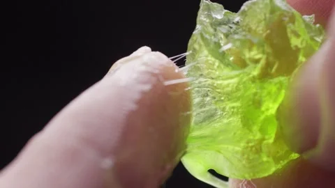 Close-up of fingers pulling a sticky, glowing green gel with an elastic texture Stock Footage 304036206