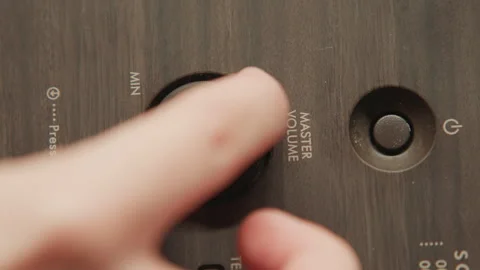 Close-up fingers rotating textured control knob on dark wood-grain device panel Stock-Footage 345656294