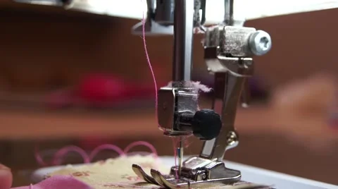 Close up fingers at sewing machine with pink thread, people in the background Stock Footage 43666247