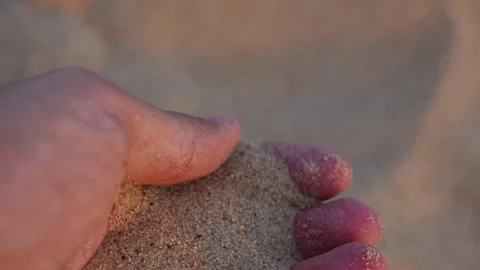 Close up of fingers sifting fine brown sand grains at sunset Stock Footage 345293496