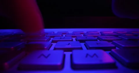 Close up of fingers typing on computer keyboard in dark room by neon lights Видео 332409146