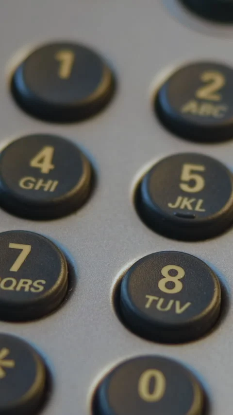 Close-up fingertip pressing numeric keypad on office desk telephone under warm Stock Footage 346987543