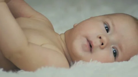 Close-up of a five month old baby lying on a white blanket and looking at ... Video stock 99076331