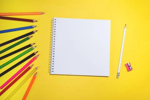 Close up flat lay with colored pencils and sketch book on yellow background. Stock Photos