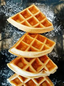 Close up flat lay of four waffles with icing sugar on black plate or dish Stock Photos