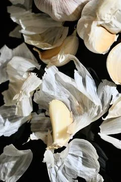 Close-up flat lay of garlic cloves, papery skins, and whole bulbs on a dark Stock Photos