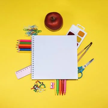 Close up flat lay with many school supplies and apple on yellow background. Stock Photos