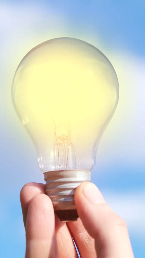 Close-up of a flickering glowing light bulb held against blue sky. Stock Footage 339620635