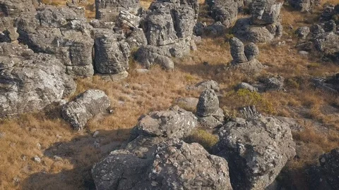 Close flight over rock formations jutting out of dry grassland Stock Footage 78584351