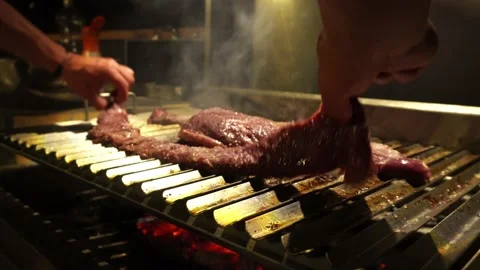 Close-up flipping a piece of grilled ribs cooking at night in 4k 库存影片 173519971