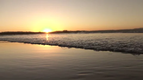 CLOSE UP: Foaming ocean waves washing smooth sandy shore at peach golden sunset Stock Footage 64959104