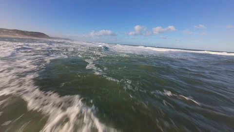Close-up of foamy surf rolling toward shore with mountain backdrop Stock Footage 344578983