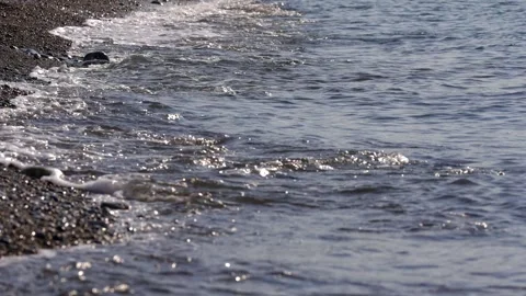Close-up of a foamy wave gently lapping at pebbles on the seashore Stock Footage 324915165