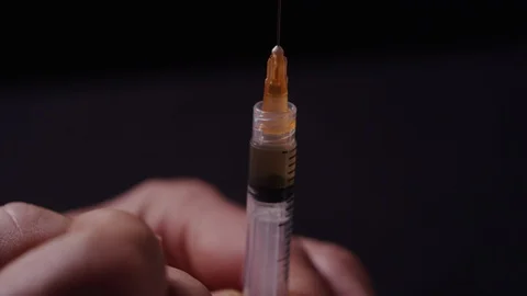 Close-up focus of a man flicking the bubbles in a syringe in a dark room Video stock 119099705