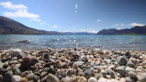 Close focus wide-angle shot of waves crashing on a pebble beach of Lake Hawea Stock-Footage 328134605