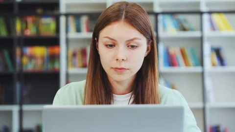 Close up of focused young woman using laptop for research in library 스톡 동영상 333331137