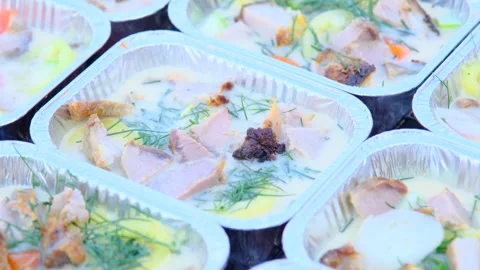 Close-up of foil tray meals with meat, vegetables, and herbs in creamy sauce Stock Footage 306463348