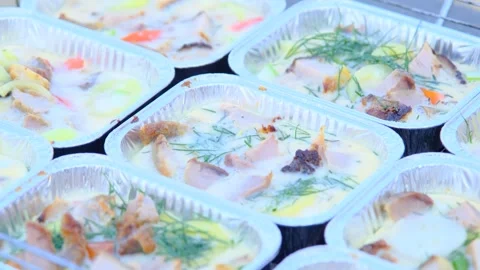 Close-up of foil tray meals with meat, vegetables, and herbs in creamy sauce Stock Footage 306463954