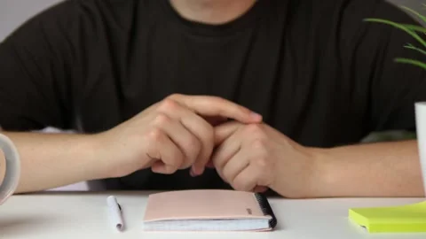 Close-up of folded hands with a notebook and pen ready for use, capturing a Stock Footage 316458846