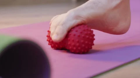 Close up of foot rolling red spiky massage ball on exercise mat Stockbeeldmateriaal 346546033