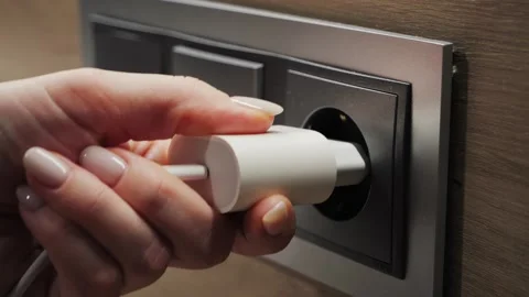 Close-up footage of hand inserting electrical plug into wall socket, connecting Stock Footage 301605791