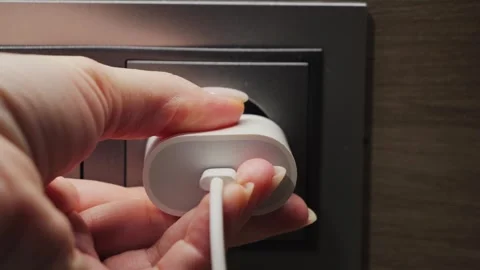 Close-up footage of hand inserting electrical plug into wall socket, connecting Stock Footage 310601299