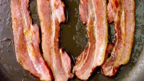 Close up footage of a slice of tasty bacon fried with oil in a cast-iron pan. 스톡 동영상 334643317