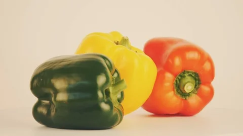 Close up footage of three paprika of different color lying on a white table Video stock 103457378