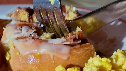 Close-up of a fork and knife cutting into a glazed cinnamon roll Stock Footage 315928372