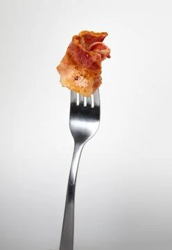 Close up of a fork with bacon on a light gray background. Stock Photos