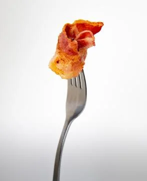 Close up of a fork with bacon on a light gray background. Stock Photos