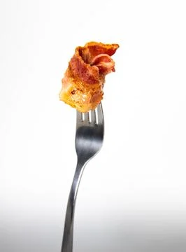 Close up of a fork with bacon on a light gray background. Stock Photos