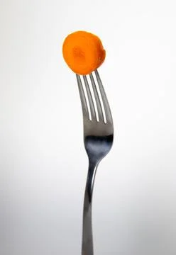 Close up of a fork with a carrot on a light gray background. Stock Photos