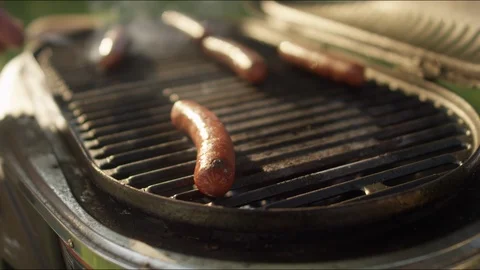 Close-up of a fork flipping hot dogs cooking on a smokey grill in slow motion Stock-Footage 125727547
