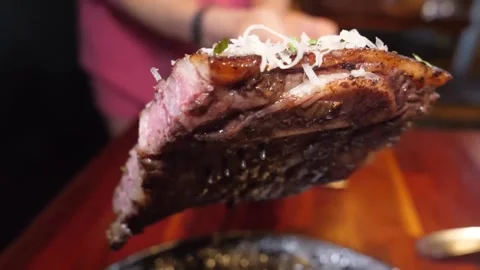 Close-up of a fork lifting a slice of medium-rare steak topped with shredded che 스톡 동영상 332817647