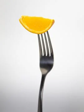 Close up of a fork with a orange on a light gray background. Stock Photos