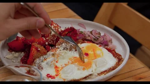 Close-up of a fork piercing a fried egg on a plate of chilaquiles with cheese Stock Footage 326369553