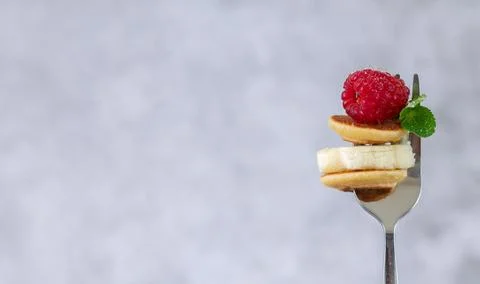 Close-up fork with tiny pancakes, banana slice, raspberry and mint leaf Stock Photos