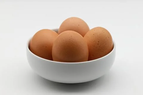 Close-up of four brown eggs nestled in a simple white bowl. Stock-Fotos