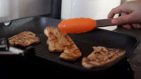 Close up frame of a hand with a meat tongs cooking some meat on a grill at ho 스톡 동영상 129043452