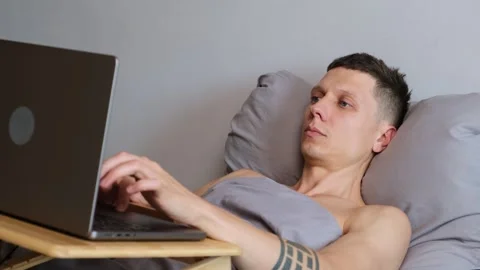 Close-up of a freelancer lying in bed working on a laptop. Calm expression Video stock 314430234