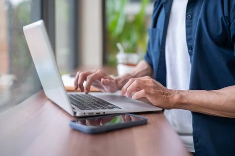 Close up of a freelancer man's hands typing on laptop beside a phone while .. Stock Photos